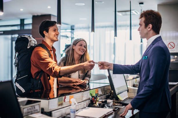 Three people, young couple travelers on hotel reception talking to male receptionist.